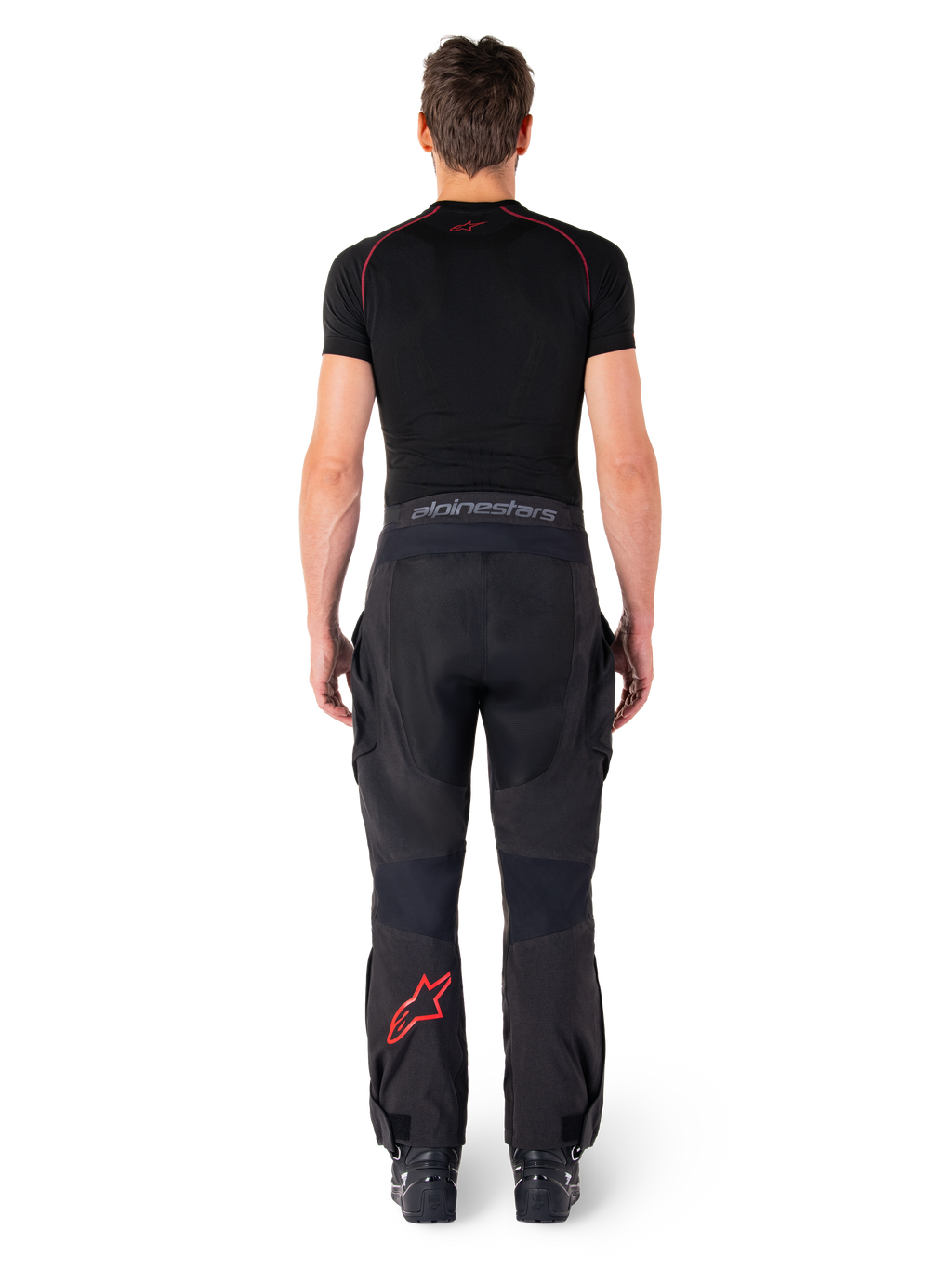 Alpinestars Hyde Xt Drystar® Pants, pantaloni da moto Adventure Touring, nero e rosso acceso, vista posteriore di un pilota che indossa i pantaloni e un base layer nero, con logo a stella rosso sulla gamba sinistra e branding grigio sulla fascia in vita.