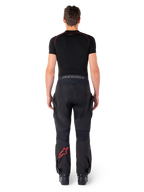 Alpinestars Hyde Xt Drystar® Pants, pantaloni da moto Adventure Touring, nero e rosso acceso, vista posteriore di un pilota che indossa i pantaloni e un base layer nero, con logo a stella rosso sulla gamba sinistra e branding grigio sulla fascia in vita.