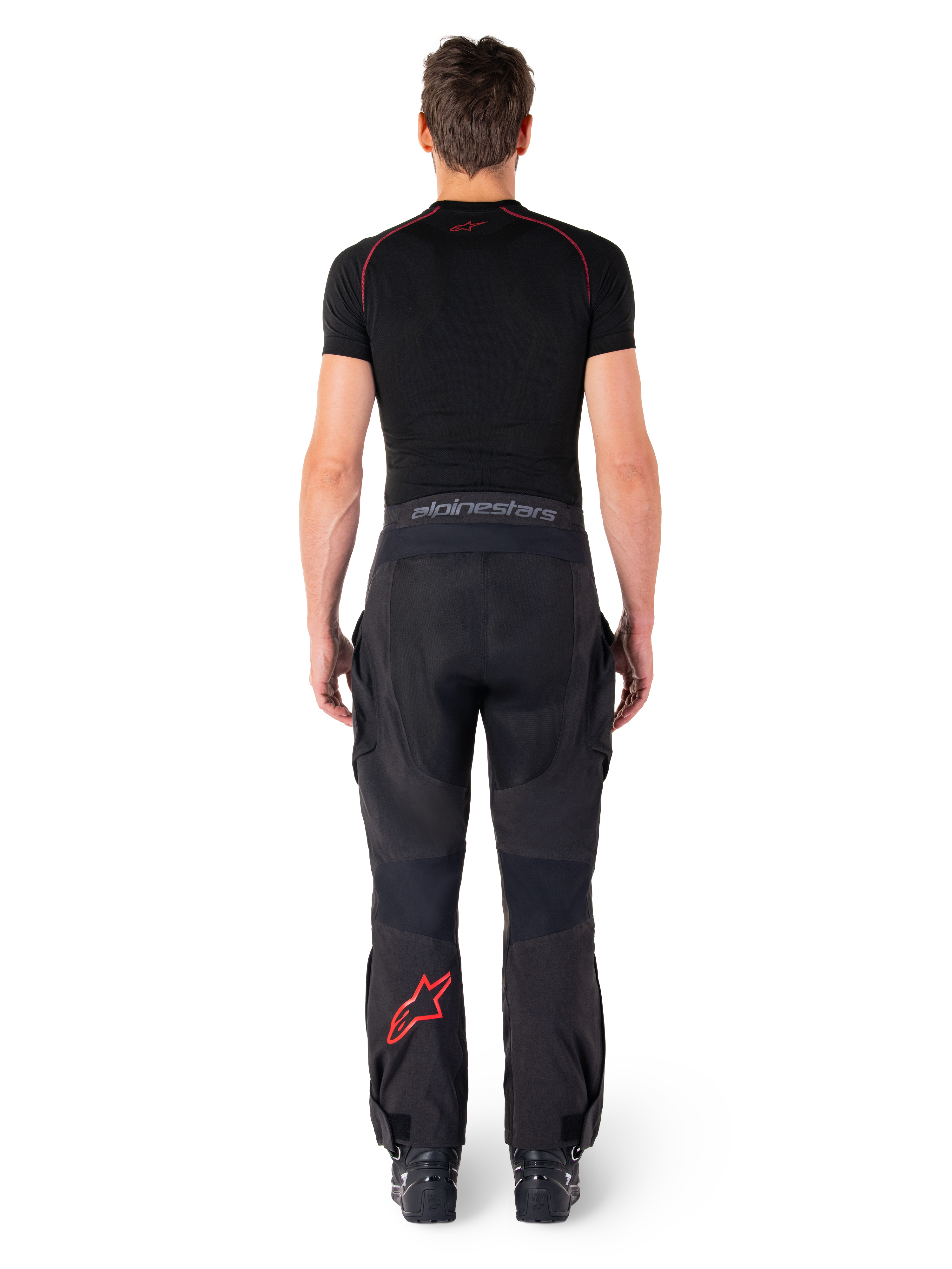 Alpinestars Hyde Xt Drystar® Pants, pantaloni da moto Adventure Touring, nero e rosso acceso, vista posteriore di un pilota che indossa i pantaloni e un base layer nero, con logo a stella rosso sulla gamba sinistra e branding grigio sulla fascia in vita.