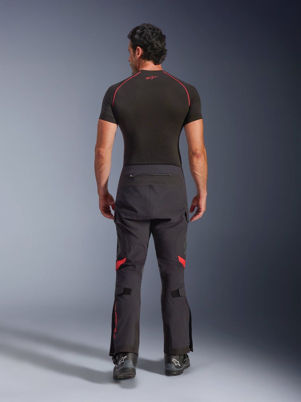 Alpinestars Halo Pro Drystar® XF Laminated Pants, pantaloni da moto adventure, Black Dark Shadow con accenti rossi, vista posteriore indossati con base layer nero a maniche corte e stivali adventure neri, costruzione laminata a 3 strati e vestibilità ergonomica