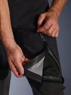 Pantaloni Alpinestars Halo Pro Drystar® XF Laminati, nero, primo piano di una persona che apre la presa d'aria sulla coscia con una cerniera impermeabile, rivelando una fodera in rete nera per la ventilazione diretta, dettaglio tecnico di pantaloni da moto adventure.