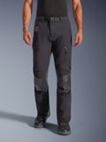 Alpinestars Halo Pro Drystar® XF Laminated Pants in Black Dark Shadow, pantaloni da moto adventure, vista frontale su modello con fibbia magnetica in vita, prese d'aria con zip sulle cosce e rinforzi in pelle sulle ginocchia, abbinati a stivali da moto neri.