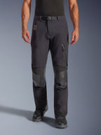 Alpinestars Halo Pro Drystar® XF Laminated Pants in Black Dark Shadow, pantaloni da moto adventure, vista frontale su modello con fibbia magnetica in vita, prese d'aria con zip sulle cosce e rinforzi in pelle sulle ginocchia, abbinati a stivali da moto neri.