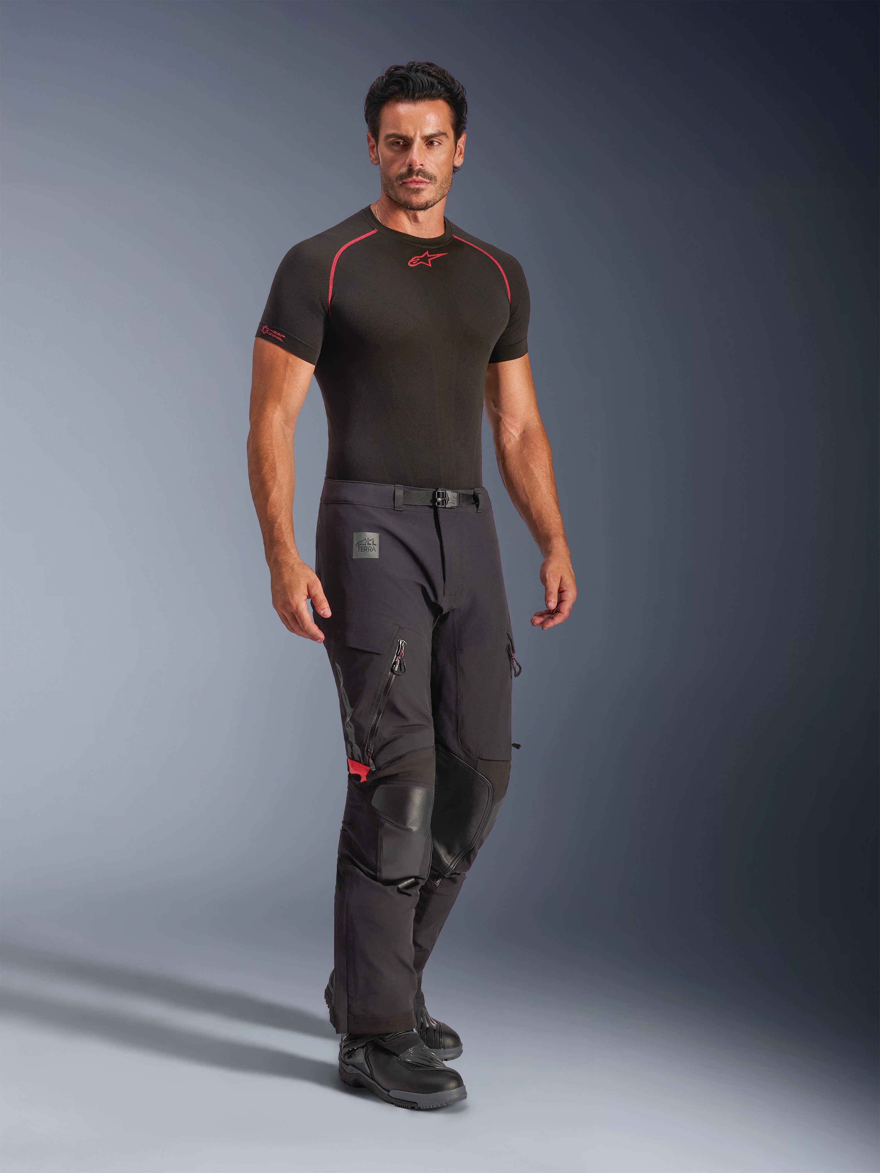 Pantaloni laminati Alpinestars Halo Pro Drystar® XF, Black Dark Shadow, pantaloni da moto adventure indossati con un base layer nero e stivali, dotati di ampie prese d'aria con zip sulle cosce, rinforzi in pelle sulle ginocchia e cintura con fibbia magnetica, progettati per prestazioni su ogni tipo di terreno