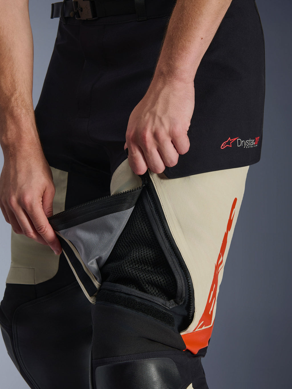 Pantaloni Alpinestars Halo Pro Drystar® XF Laminati, Mastic Black, dettaglio ravvicinato della presa d'aria sulla coscia con cerniera aperta per mostrare il pannello interno in rete per il flusso d'aria, con logo Drystar XF rosso e dettagli grafici arancioni