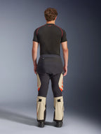 Pantaloni laminati Alpinestars Halo Pro Drystar® XF, Mastic Black, vista posteriore su un modello, design a blocchi di colore nero e beige con loghi arancioni, pantaloni da moto adventure touring con robusta struttura in tessuto e sezioni regolabili sui polpacci