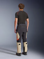 Pantaloni laminati Alpinestars Halo Pro Drystar® XF, pantaloni da moto adventure, Mastic Black e Tan con accenti arancioni, vista posteriore che mostra la costruzione del guscio laminato a 3 strati, abbinati a un base layer nero e stivali adventure.