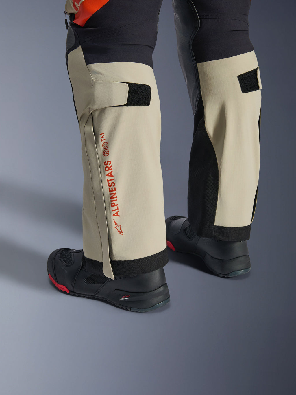 Alpinestars Halo Pro Drystar® XF Laminated Pants, Mastic Black, primo piano della parte inferiore delle gambe con logo Alpinestars rosso e regolatori del polpaccio in velcro, indossati con stivali da avventura neri