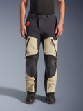 Alpinestars Halo Pro Drystar® XF Laminated Pants, pantaloni da moto adventure, Mastic Black, vista frontale indossati da un pilota, con ampie prese d'aria con cerniera sulle cosce, pannelli rinforzati neri sulle ginocchia e costruzione in tessuto color sabbia, abbinati a stivali da moto neri e rossi