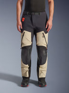Alpinestars Halo Pro Drystar® XF Laminated Pants, pantaloni da moto adventure, Mastic Black, vista frontale indossati da un pilota, con ampie prese d'aria con cerniera sulle cosce, pannelli rinforzati neri sulle ginocchia e costruzione in tessuto color sabbia, abbinati a stivali da moto neri e rossi