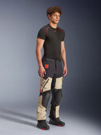 Alpinestars Halo Pro Drystar® XF Laminated Pants in Mastic Black, pantaloni da moto adventure indossati da un modello, con rinforzi neri su ginocchia e seduta, branding arancione e molteplici cerniere funzionali, abbinati a un base layer nero e stivali da moto.