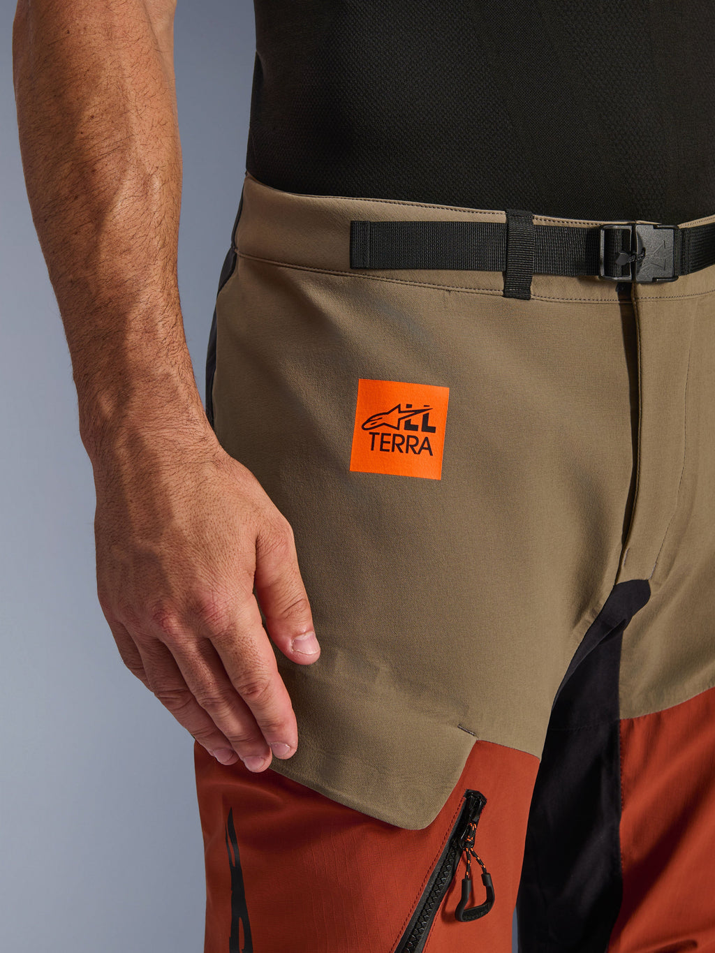 Alpinestars Halo Pro Drystar® XF Laminated Pants, Walnut Rust Black, primo piano della parte superiore della coscia con una toppa arancione brillante del logo All Terra, pannelli color noce e ruggine e una cintura nera in vita con fibbia magnetica, abbigliamento da moto adventure