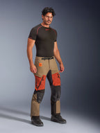 Alpinestars Halo Pro Drystar® XF Laminated Pants, pantaloni da moto Adventure, Walnut Rust e nero, indossati da un modello con base layer a compressione nero e stivali neri, con pannelli rinforzati sulle ginocchia, prese d'aria sulle cosce con zip arancioni e marchio Terra, abbigliamento tecnico per tutti i terreni