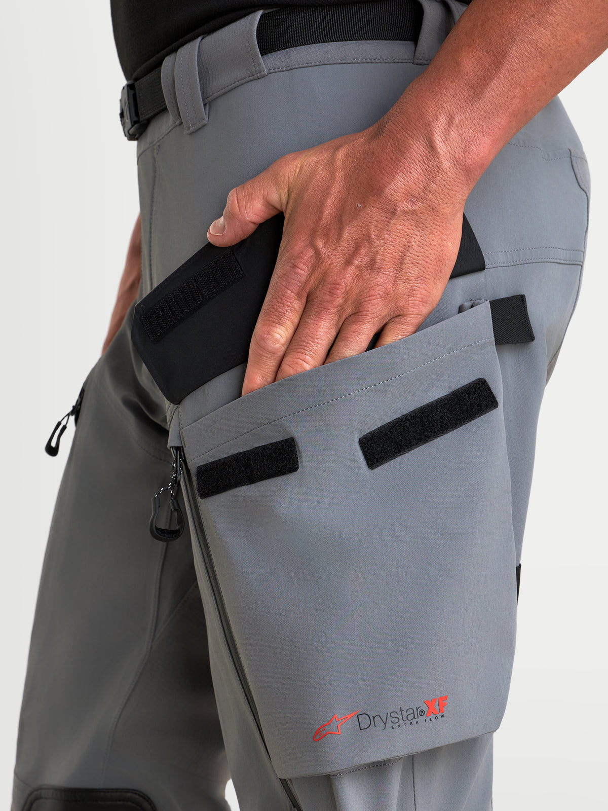 Alpinestars Maxdura Drystar XF Laminated Pantaloni, pantaloni da moto adventure, grigio scuro e nero, dettaglio della mano che accede alla tasca cargo inclinata sulla coscia con marchio Drystar XF