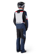 Vista posteriore di un motociclista con pantaloni impermeabili Alpinestars ST-1 e giacca coordinata in blu scuro, nero e rosso brillante, abbigliamento adventure touring con pannelli in tessuto e dettagli riflettenti, casco e stivali neri.
