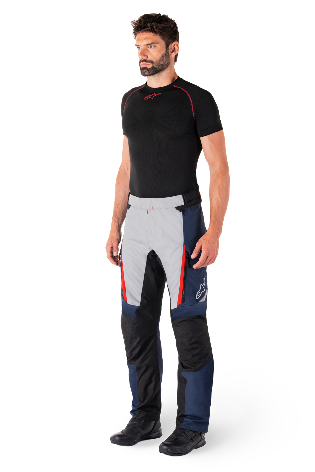 Pantaloni Alpinestars St-1 Waterproof, pantaloni da moto touring, blu scuro, nero e rosso acceso, indossati da un modello con base layer nero e stivali neri, con tasche con cerniera e logo Alpinestars sulla gamba