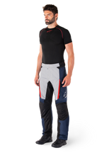 Pantaloni Alpinestars St-1 Waterproof, pantaloni da moto touring, blu scuro, nero e rosso acceso, indossati da un modello con base layer nero e stivali neri, con tasche con cerniera e logo Alpinestars sulla gamba