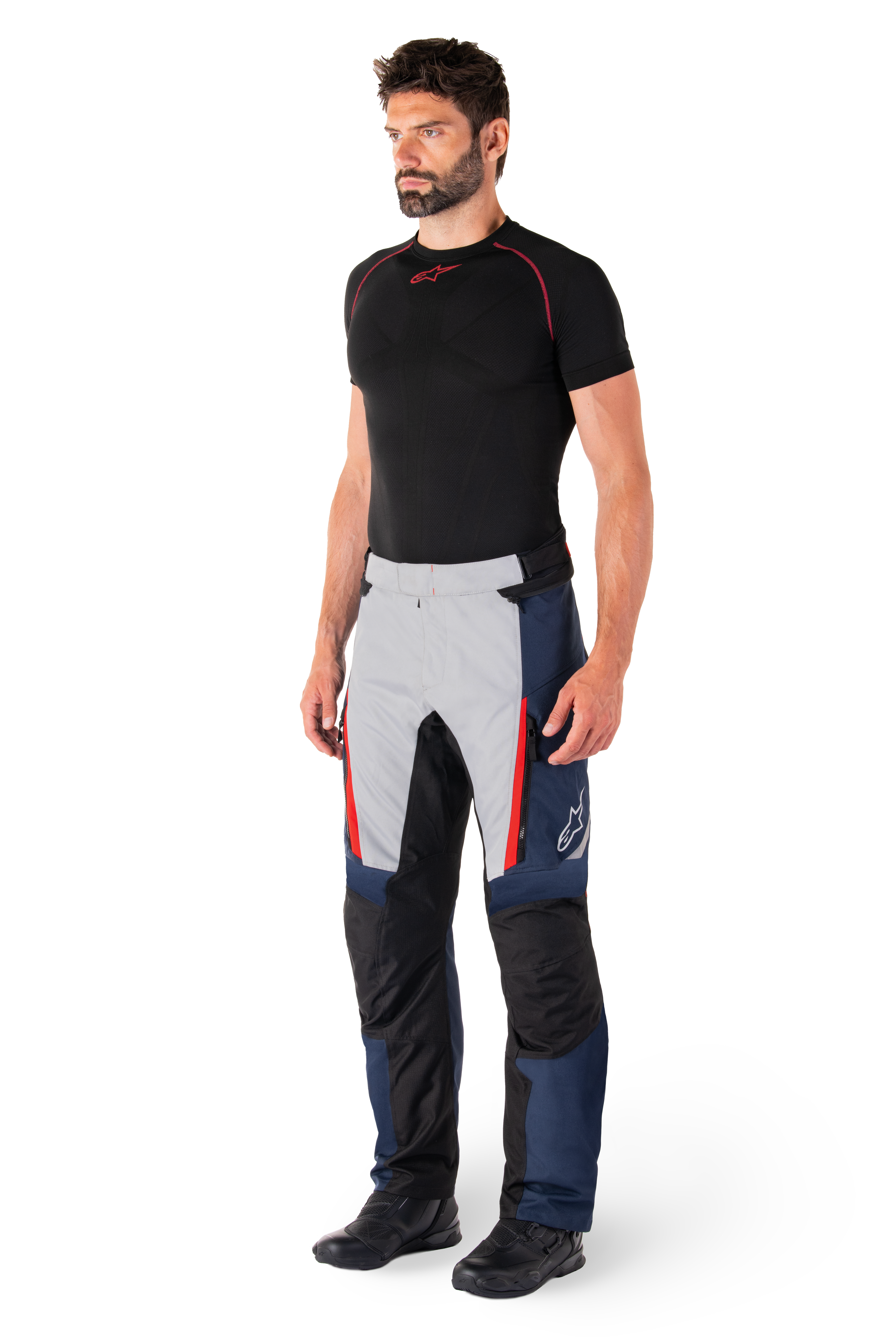 Pantaloni Alpinestars St-1 Waterproof, pantaloni da moto touring, blu scuro, nero e rosso acceso, indossati da un modello con base layer nero e stivali neri, con tasche con cerniera e logo Alpinestars sulla gamba