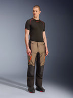Alpinestars Andes V4 Drystar® Pants, pantaloni da moto adventure touring, Walnut Black con accenti arancioni, indossati da un modello con base layer nero a maniche corte e stivali neri, con pannelli in tessuto rinforzato e tasche cargo, design robusto per la guida in ogni condizione atmosferica