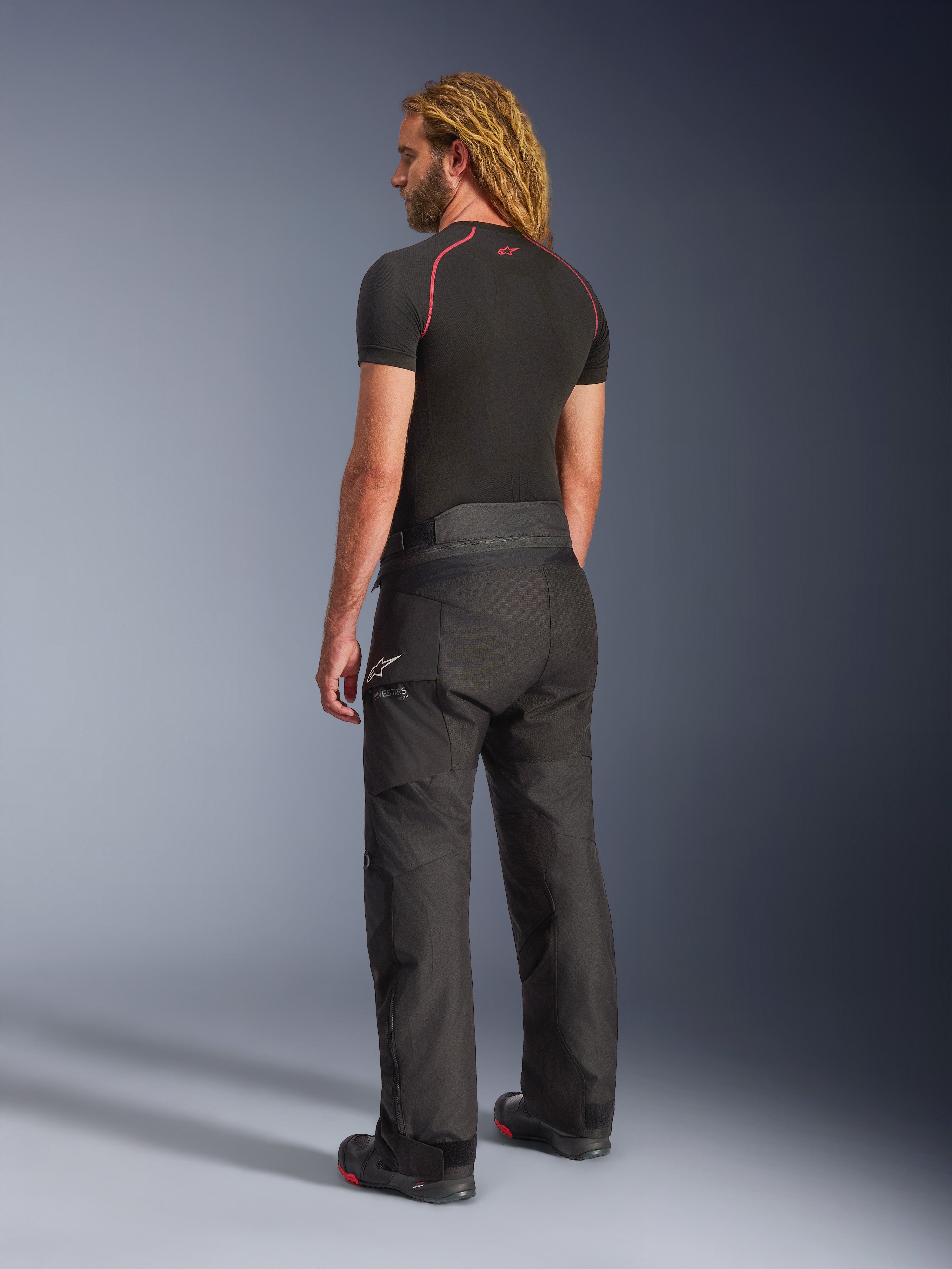 Alpinestars Andes V4 Drystar® Pants - Lunghi, pantaloni da moto adventure, nero, vista posteriore di tre quarti su modello, design in tessuto resistente con pannelli rinforzati su seduta e ginocchia, logo a stella Alpinestars, indossati con base layer nero e stivali da moto
