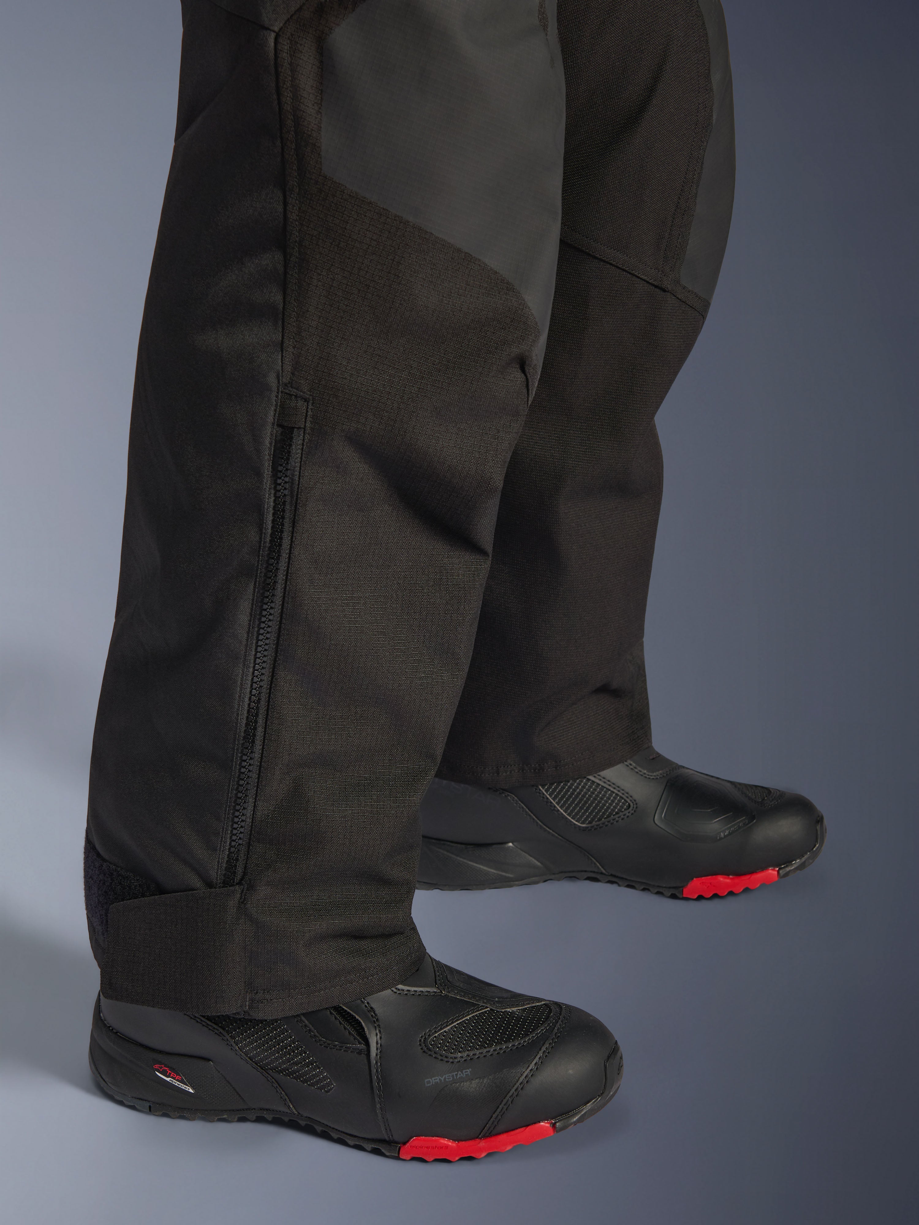 Alpinestars Pantaloni Andes V4 Drystar® - Short, nero, primo piano del dettaglio della parte inferiore della gamba che mostra la costruzione in tessuto, cerniera verticale per la ventilazione e polsini regolabili alle caviglie, indossati con stivali da moto neri