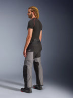 Alpinestars Andes V4 Drystar® Pants, pantaloni da moto adventure, nero e grigio scuro, indossati con base layer nero a maniche corte e stivali da moto neri, vista laterale e posteriore con design in tessuto multi-pannello e logo Alpinestars sulla coscia.