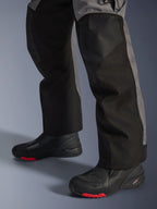 Pantaloni Alpinestars Andes V4 Drystar®, pantaloni da moto in tessuto, nero e grigio scuro, indossati con stivali da moto neri con suole rosse, design adventure touring con pannelli delle gambe rinforzati e vestibilità a taglio dritto.
