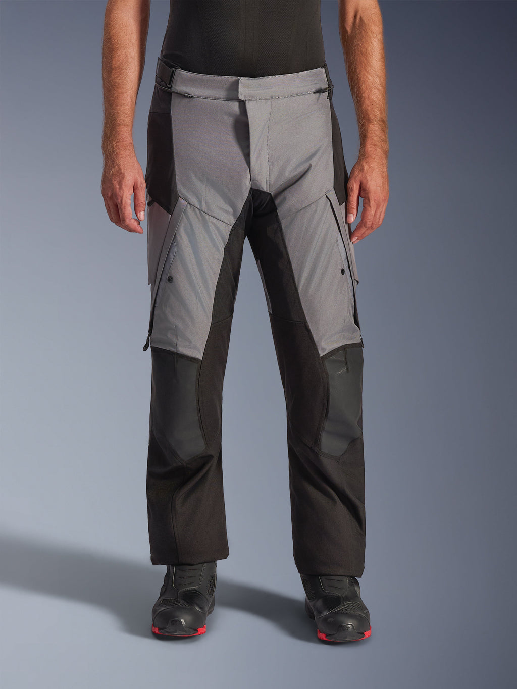 Alpinestars Andes V4 Drystar® Pants, pantaloni da moto adventure touring, grigio e nero, vista frontale indossati da un modello con stivali da guida neri, caratterizzati da rinforzi sulle ginocchia e tasche cargo sulle cosce, costruzione in tessuto impermeabile e traspirante per tutte le condizioni atmosferiche
