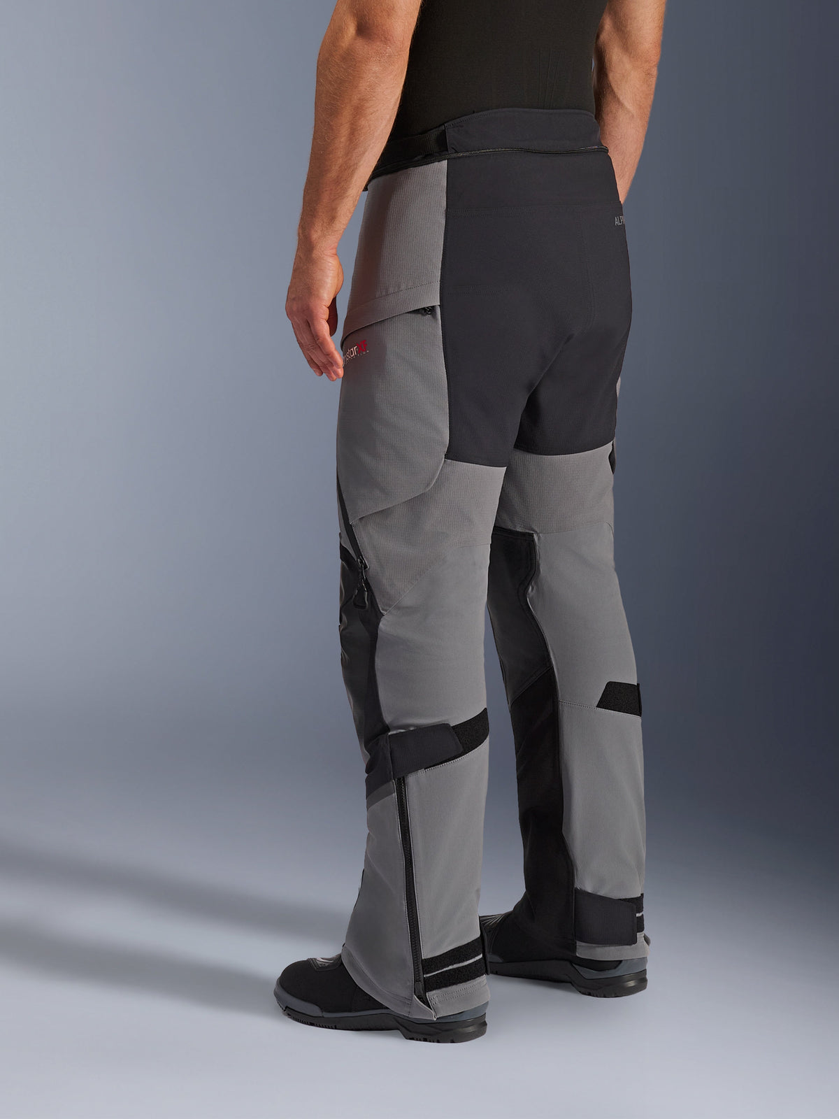 Pantaloni Alpinestars Andes Pro Drystar® XF, pantaloni da moto adventure, grigio scuro e nero, vista posteriore di tre quarti, struttura in tessuto con rinforzi neri su seduta e interno gamba, fondo gamba con cerniera e linguette regolabili