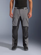 Alpinestars Andes Pro Drystar® XF Pants, pantaloni da moto, grigio scuro e nero, vista frontale, con pannelli rinforzati neri sulle ginocchia, cerniere impermeabili e cintura con fibbia magnetica, indossati con stivali neri