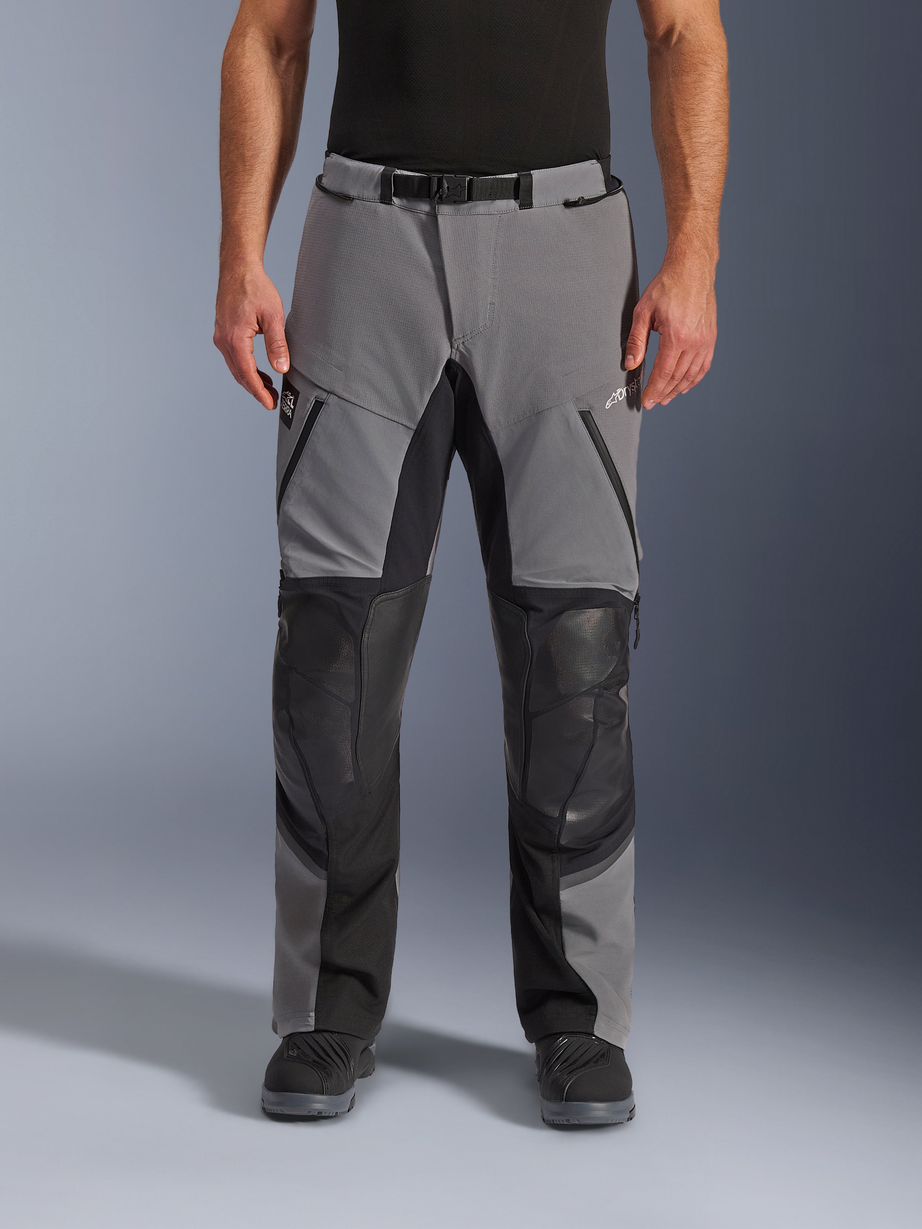 Alpinestars Andes Pro Drystar® XF Pants, pantaloni da moto, grigio scuro e nero, vista frontale, con pannelli rinforzati neri sulle ginocchia, cerniere impermeabili e cintura con fibbia magnetica, indossati con stivali neri