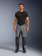 Alpinestars Andes Pro Drystar® XF Pants, pantaloni da moto adventure, grigio scuro e nero, vista frontale indossati da un modello con uno strato base nero, con pannelli rinforzati sulle ginocchia e tasche con zip impermeabili