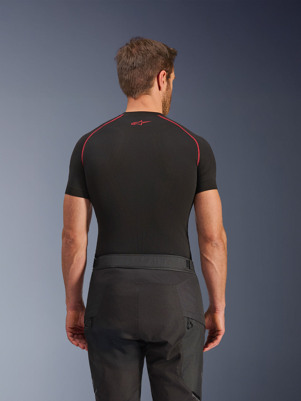 Pantaloni Alpinestars Cusco Drystar®, pantaloni da moto neri, vista posteriore di un pilota che indossa abbigliamento adventure touring con una maglia a compressione nera a maniche corte e cuciture rosse, robusta costruzione in tessuto ripstop e 600D.