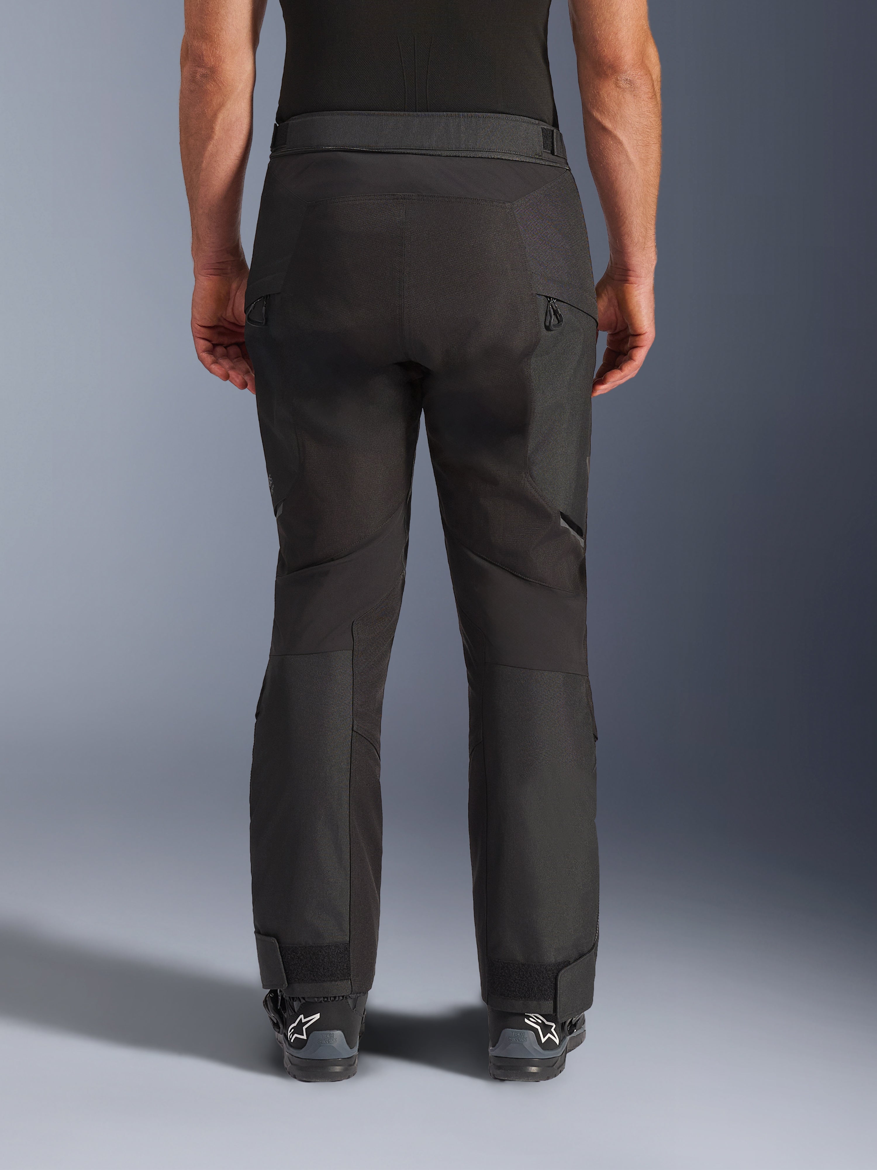 Pantaloni Alpinestars Cusco Drystar®, pantaloni da moto, nero, vista posteriore indossati da un pilota, con pannelli in tessuto testurizzato, prese d'aria con cerniera sulle cosce e chiusure regolabili alle caviglie, abbinati a stivali Alpinestars neri.