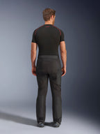 Pilota che indossa i pantaloni Alpinestars Cusco Drystar®, pantaloni da moto adventure neri, vista posteriore, abbinati a una maglia a compressione nera a maniche corte e stivali da moto neri, caratterizzati da un design in tessuto resistente con pannelli articolati per il touring