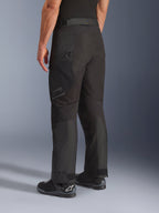 Pantaloni Alpinestars Cusco Drystar®, pantaloni da moto, nero, vista posteriore a tre quarti che mostra la tasca sulla coscia con cerniera e i pannelli articolati, indossati con stivali da moto neri, design resistente per adventure touring con branding discreto