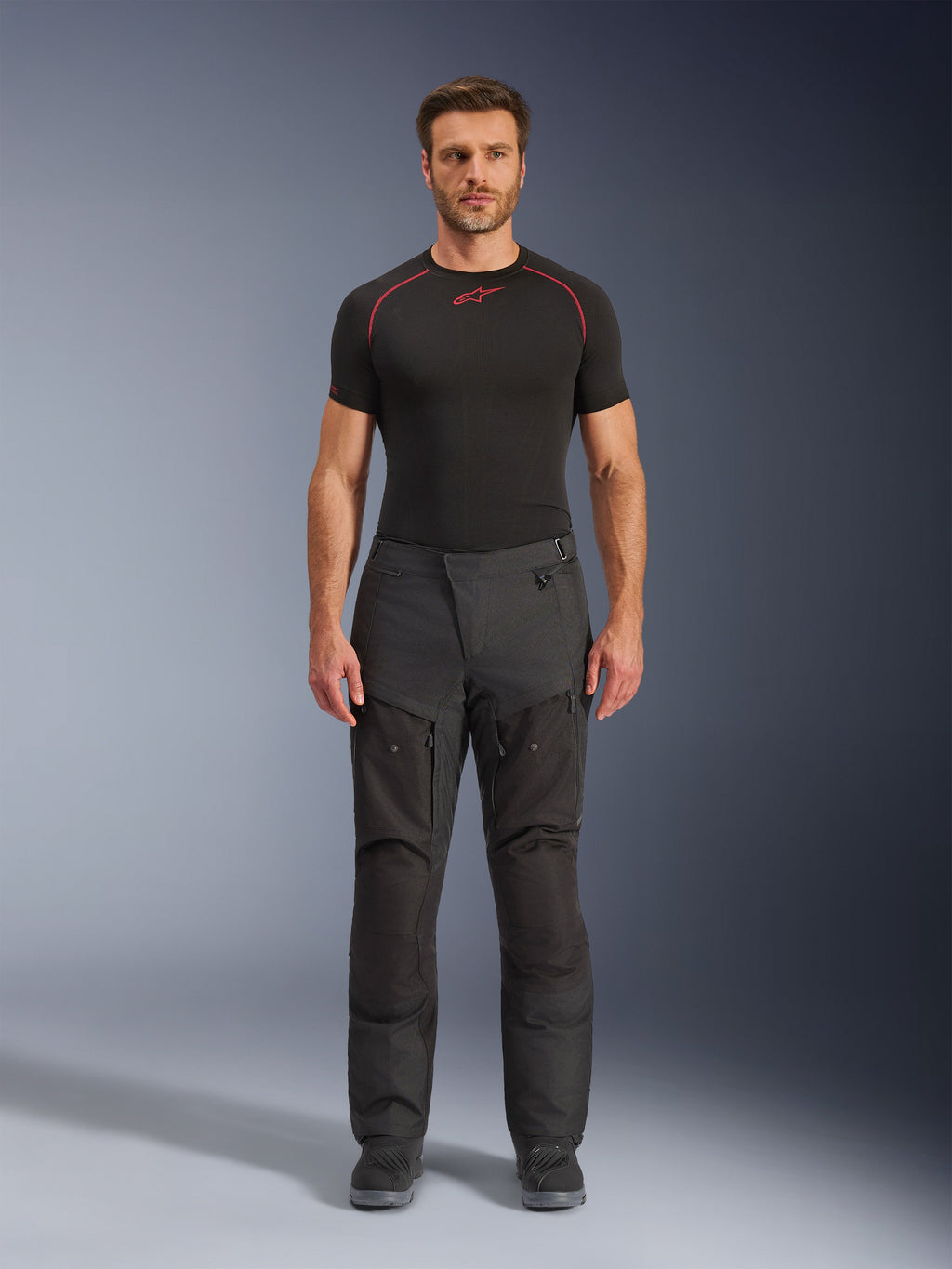 Pantaloni Alpinestars Cusco Drystar®, pantaloni da moto in tessuto, nero, indossati da un modello con base layer e stivali neri, design adventure touring con pannelli di ventilazione con zip sulle cosce e costruzione multi-pannello resistente