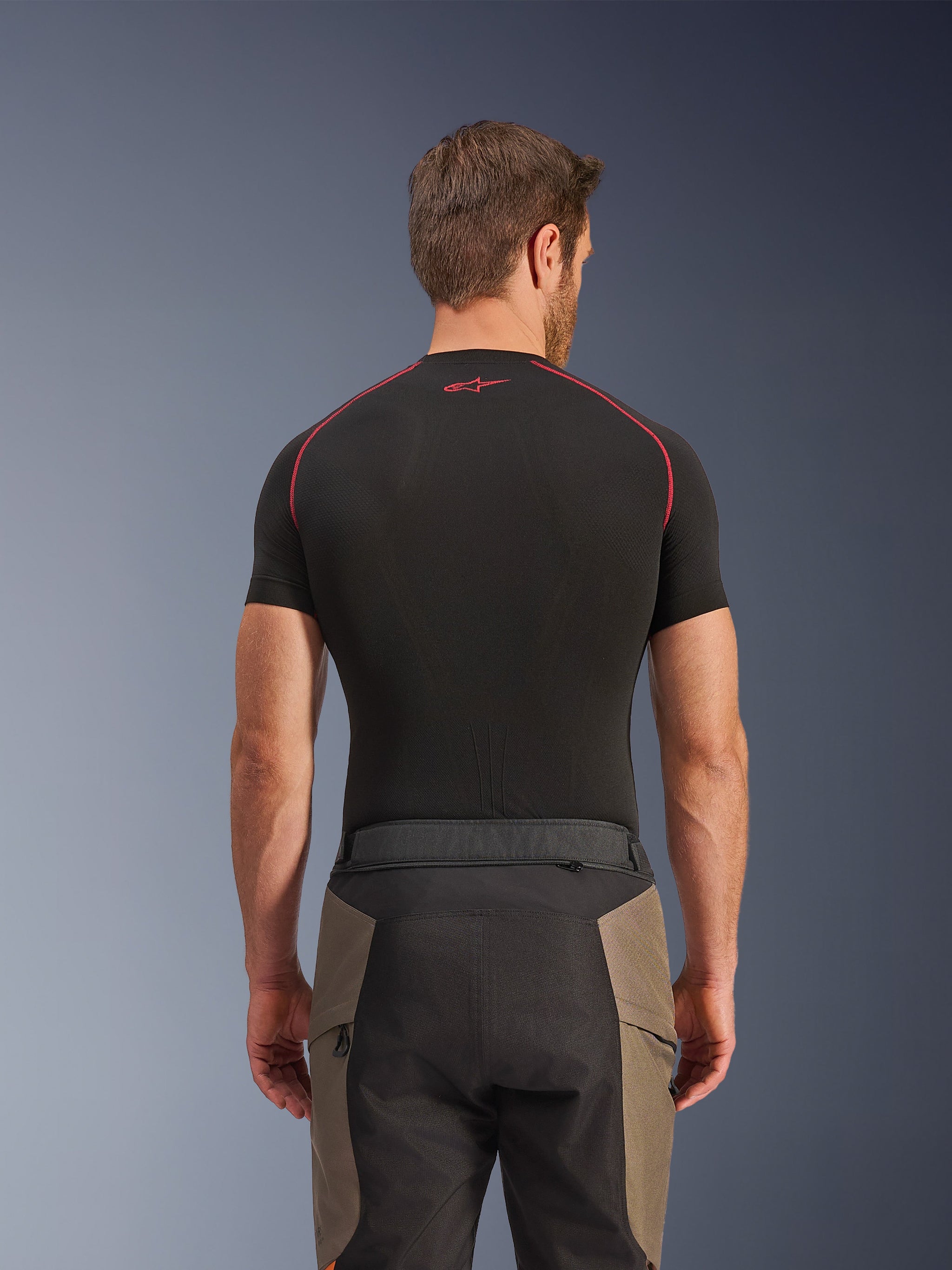 Alpinestars Pantaloni Cusco Drystar®, pantaloni da adventure touring, Walnut Black, vista posteriore con dettagli della vita e design color-block, indossati con un base layer nero a maniche corte con cuciture rosse e logo
