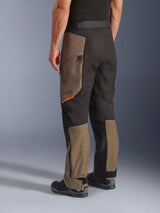 Alpinestars Cusco Drystar® Pants, pantaloni da moto adventure, colore Walnut Black con un piccolo accento arancione, vista posteriore a tre quarti che mostra la costruzione in tessuto e i pannelli color noce, indossati con stivali da moto neri.