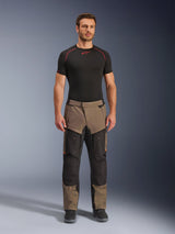 Pantaloni Alpinestars Cusco Drystar®, Walnut Black, pantaloni da moto adventure touring, indossati da un modello con base layer nero e stivali neri, con pannelli neri e color noce, dettagli arancioni e cerniere di ventilazione sulle cosce.