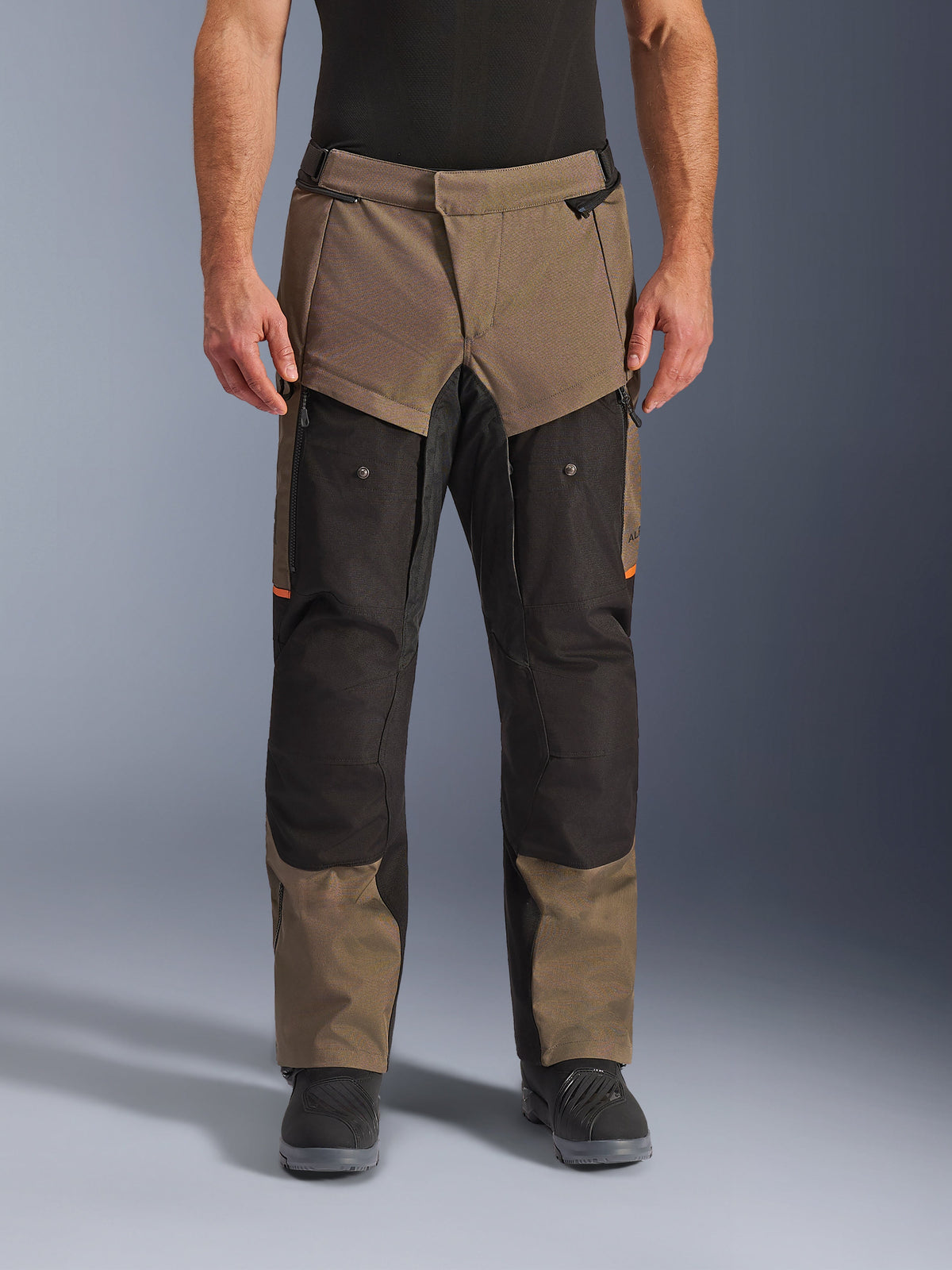 Pantaloni Alpinestars Cusco Drystar®, pantaloni da moto adventure touring, noce e nero con accenti arancioni, vista frontale su modello, caratterizzati da costruzione in tessuto tecnico, tasche cargo e cerniere di ventilazione, indossati con stivali da moto neri