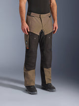 Alpinestars Cusco Drystar® Pants, pantaloni da moto adventure, Walnut Black, indossati da un modello con stivali neri, caratterizzati da un design a pannelli multipli marrone e nero con tasche con cerniera e ginocchia rinforzate per il touring