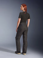 Pantaloni Alpinestars Stella Andes V4 Drystar®, neri, pantaloni da moto adventure, vista laterale posteriore su una modella, abbinati a t-shirt nera e stivali, tasche cargo laterali con logo bianco e struttura in tessuto resistente