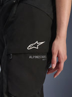 Pantaloni Alpinestars Stella Andes V4 Drystar®, pantaloni da moto da donna, neri, primo piano della tasca cargo sulla coscia con logo a stella bianco e branding, materiale tessile resistente per adventure touring