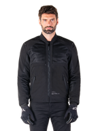 Parka impermeabile Alpinestars Mootant, giacca da moto nera, vista frontale su modello maschile, caratterizzata da una costruzione tessile modulare con pannelli in rete per la ventilazione, colletto a costine e tasche con zip, indossata con guanti neri con marchio Alpinestars bianco