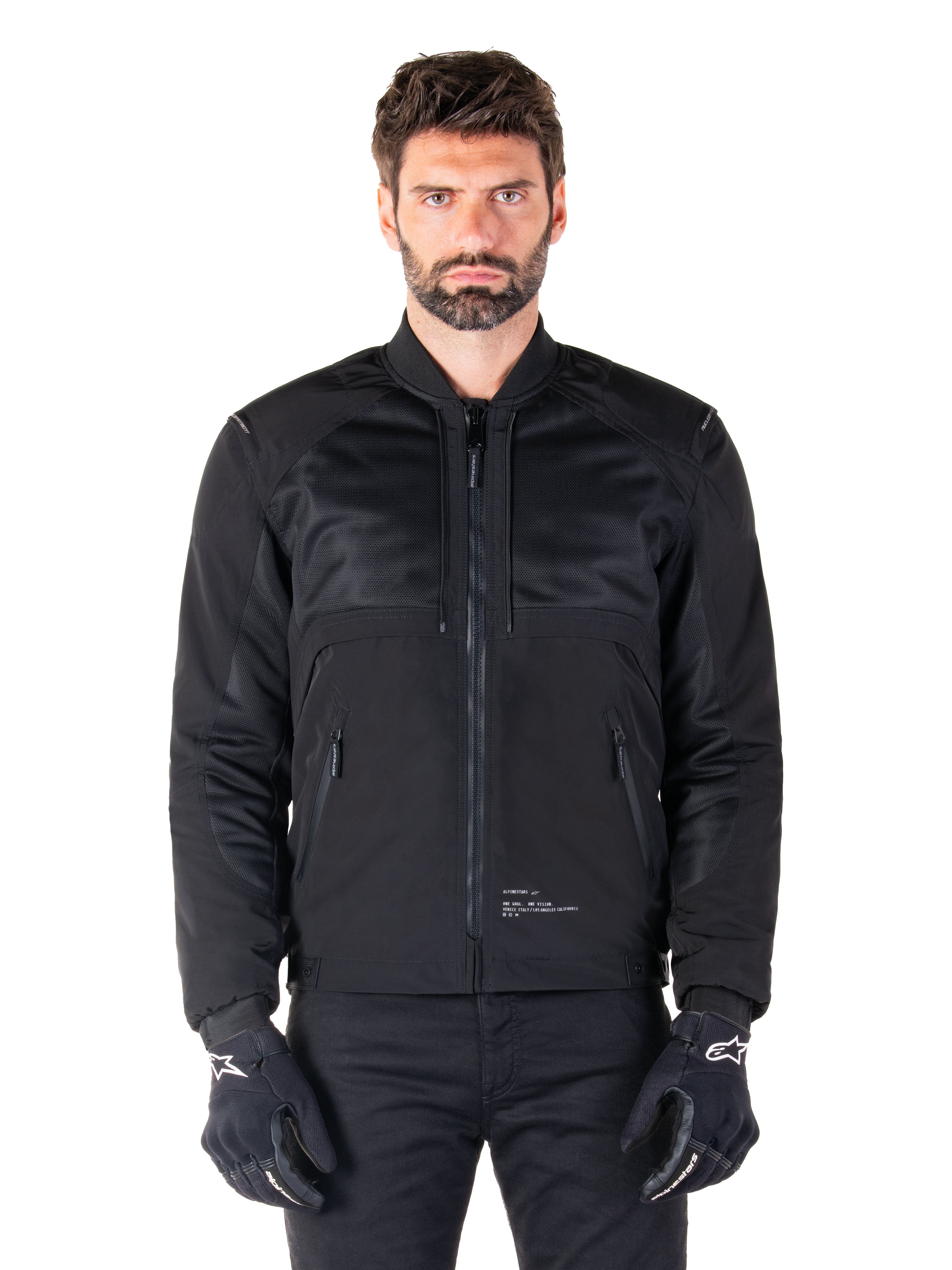 Parka impermeabile Alpinestars Mootant, giacca da moto nera, vista frontale su modello maschile, caratterizzata da una costruzione tessile modulare con pannelli in rete per la ventilazione, colletto a costine e tasche con zip, indossata con guanti neri con marchio Alpinestars bianco