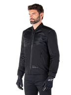 Parka Alpinestars Mootant Waterproof, giacca da moto modulare nera mostrata nella sua configurazione bomber con pannelli in rete sulla parte superiore del corpo e colletto a costine, indossata da un modello con guanti e pantaloni da guida neri, stile streetwear contemporaneo urbano.