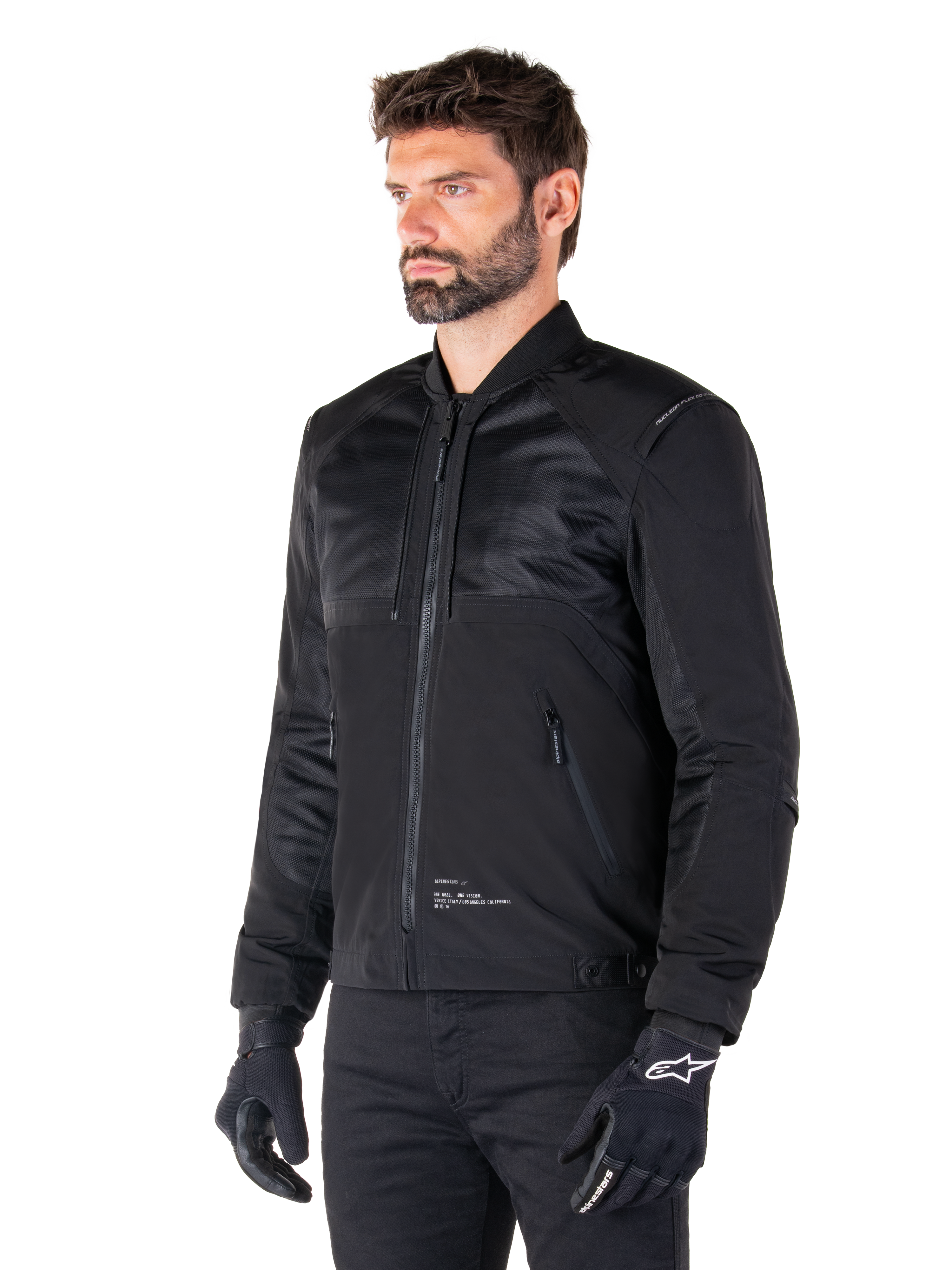 Parka Alpinestars Mootant Waterproof, giacca da moto modulare nera mostrata nella sua configurazione bomber con pannelli in rete sulla parte superiore del corpo e colletto a costine, indossata da un modello con guanti e pantaloni da guida neri, stile streetwear contemporaneo urbano.