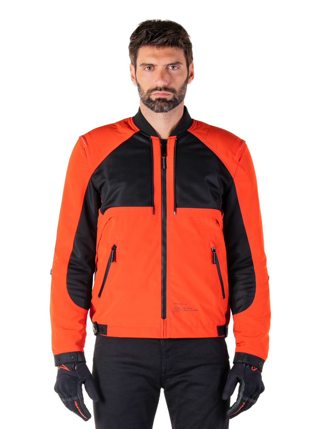 Alpinestars Mootant Waterproof Parka in Spicy Orange e nero, giacca da moto modulare mostrata in configurazione stile bomber su un modello maschile, con pannelli in rete nera sulla parte superiore del torace, busto e maniche arancione acceso, cerniera frontale e colletto a costine, abbinata a guanti e pantaloni neri