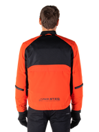 Alpinestars Parka impermeabile Mootant, giacca da moto, arancione e nero, vista posteriore, con parte superiore della schiena in mesh nero e pannello inferiore arancione con logo MO.ST.EQ., indossato con pantaloni e guanti neri